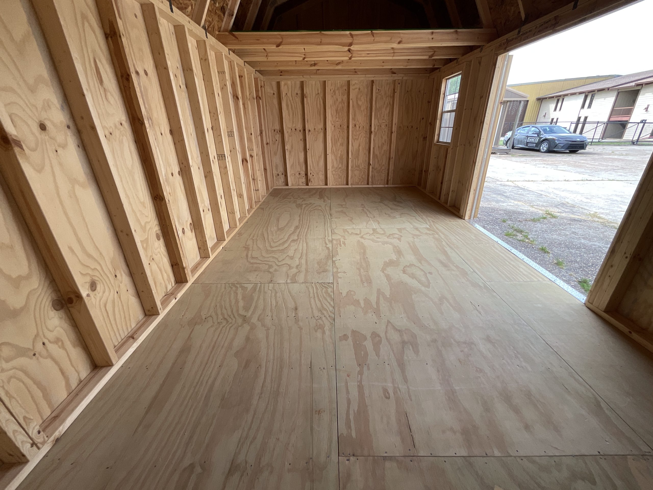 Interior view of 10x20 side lofted barn with open floor space. Plywood flooring inside portable shed with visible grain.
